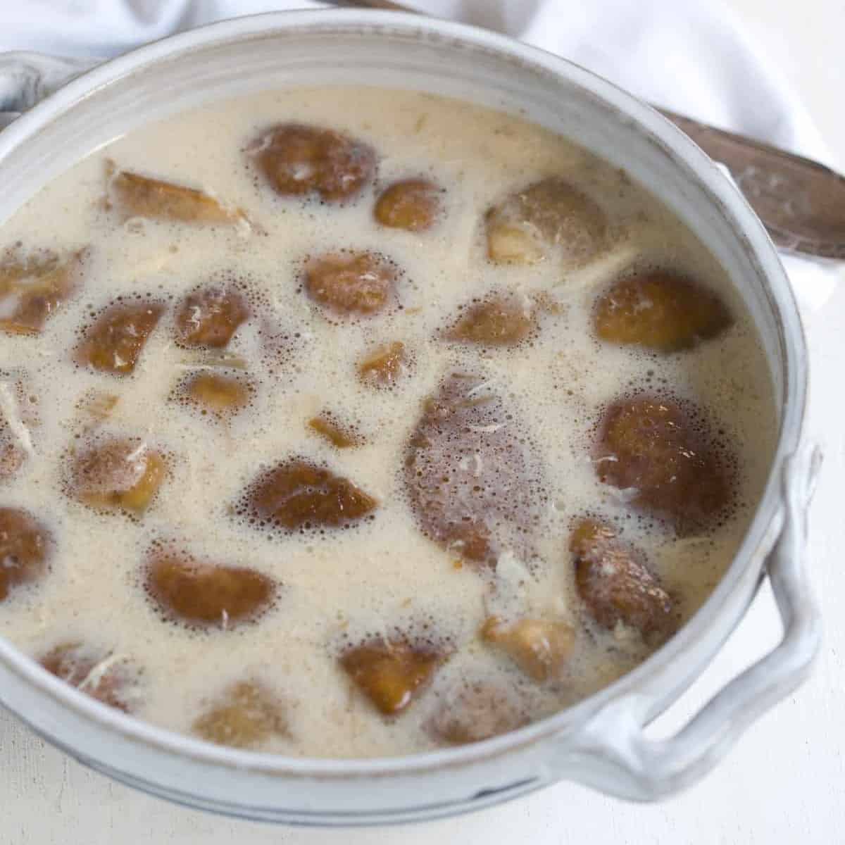 Bílá houbová polévka se smetanou, nakyslá, servírovaná v misce.